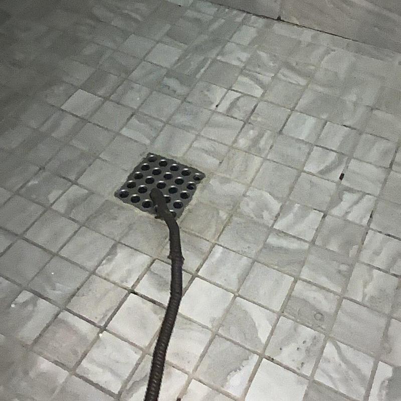 Shower drain with snake tool on tiled floor