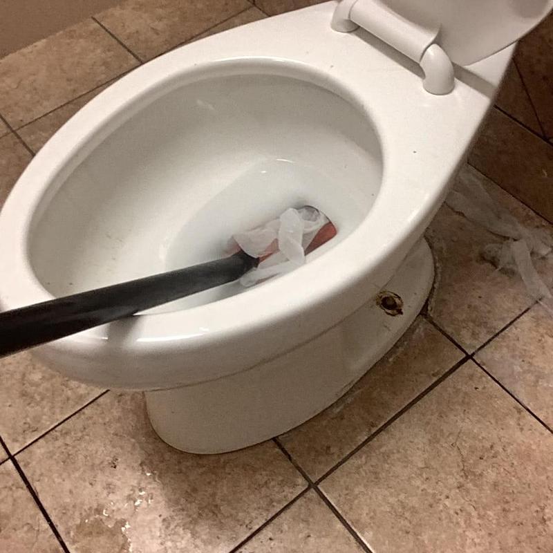 Toilet auger clearing blockage in men's bathroom restroom