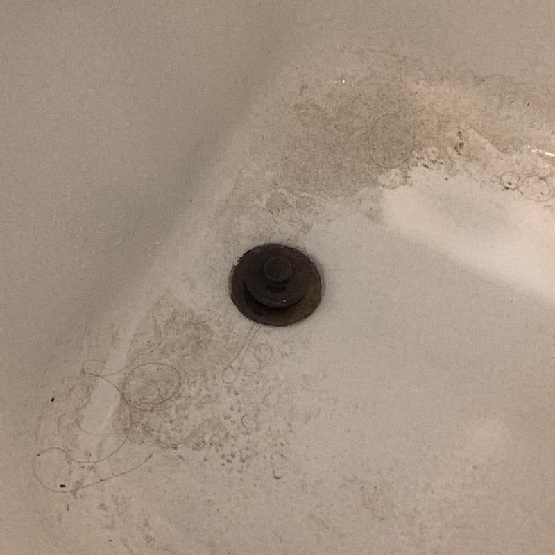 Tub drain with grime and hair buildup in bathtub