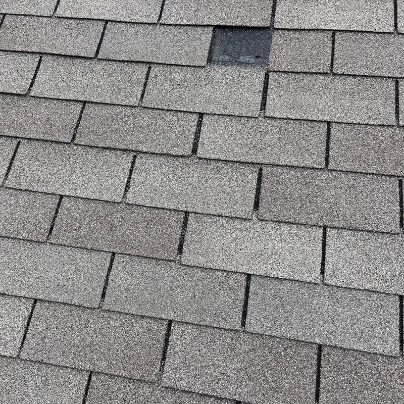Asphalt roof shingles with damaged patch visible Asphalt roof shingles with damaged patch visible