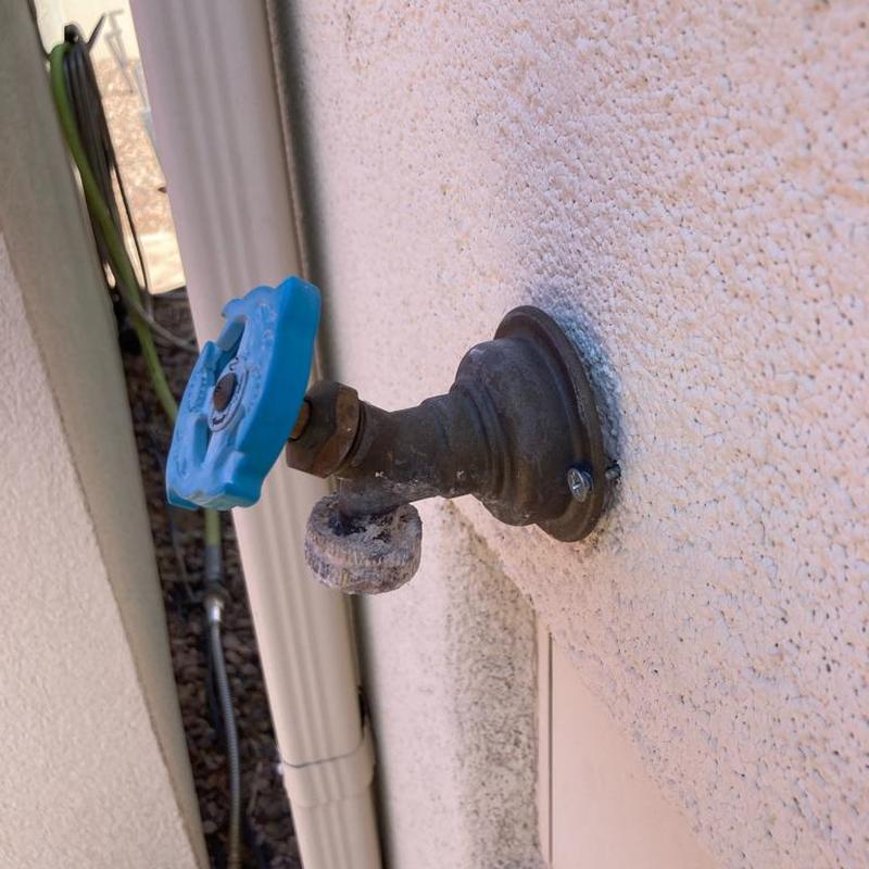 Outdoor hose bib with blue handle on stucco wall