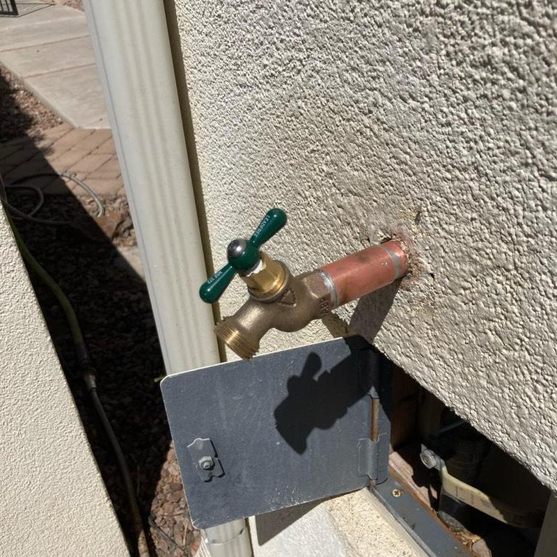 Hose bib with green handle on stucco wall
