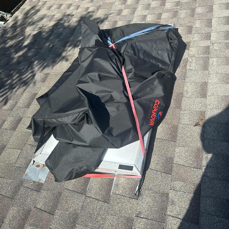 Roof vent covered with protective tarp and straps on shingles