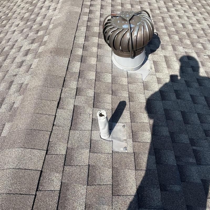 Roof vent pipe on shingled residential roof next to turbine vent