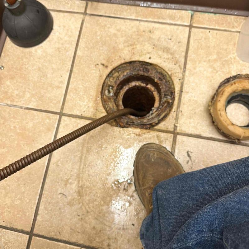 Toilet flange and drain pipe with auger on tiled floor