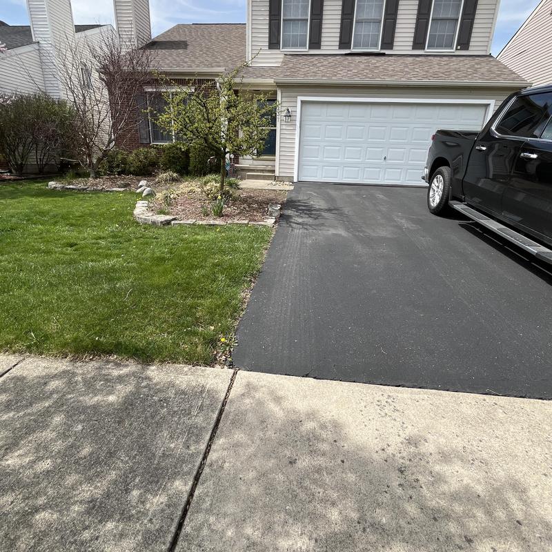 Asphalt driveway sealing with adjacent lawn and house Asphalt driveway sealing with adjacent lawn and house