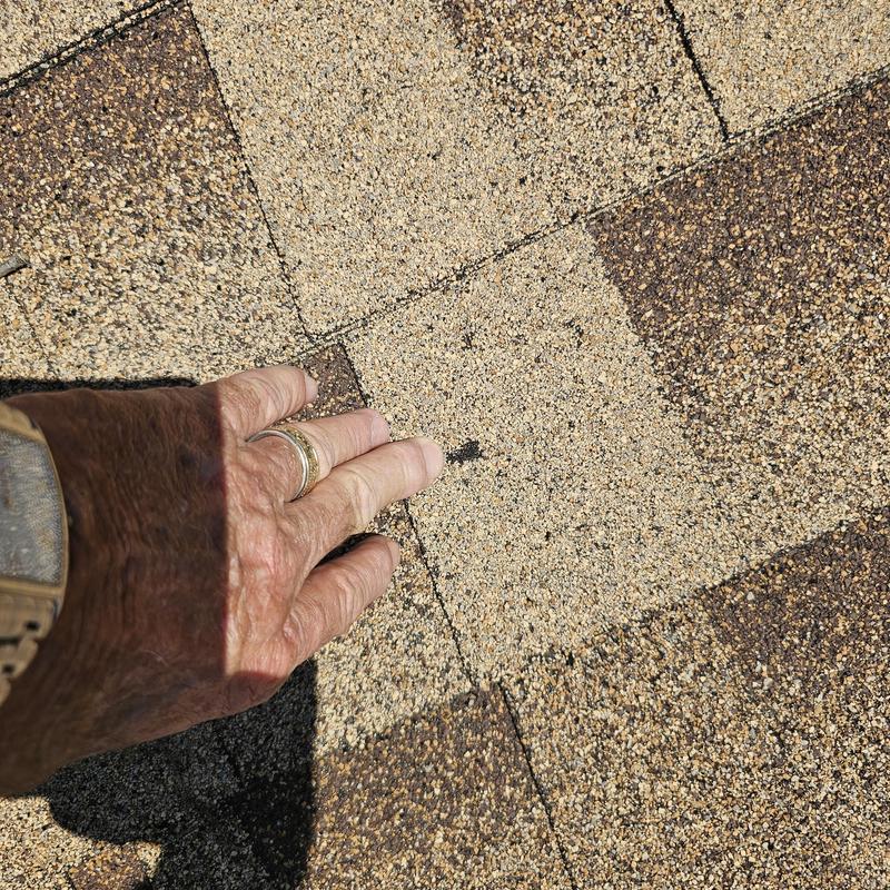 Asphalt shingles with hail damage close-up and hand