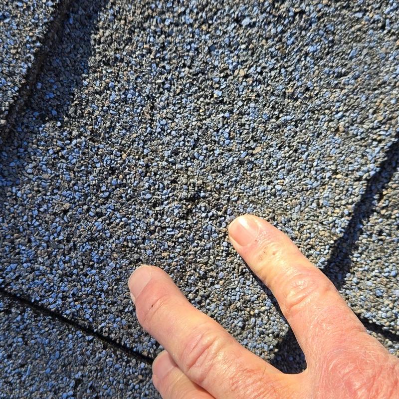 Roof shingles with hail damage close-up and hand pointing