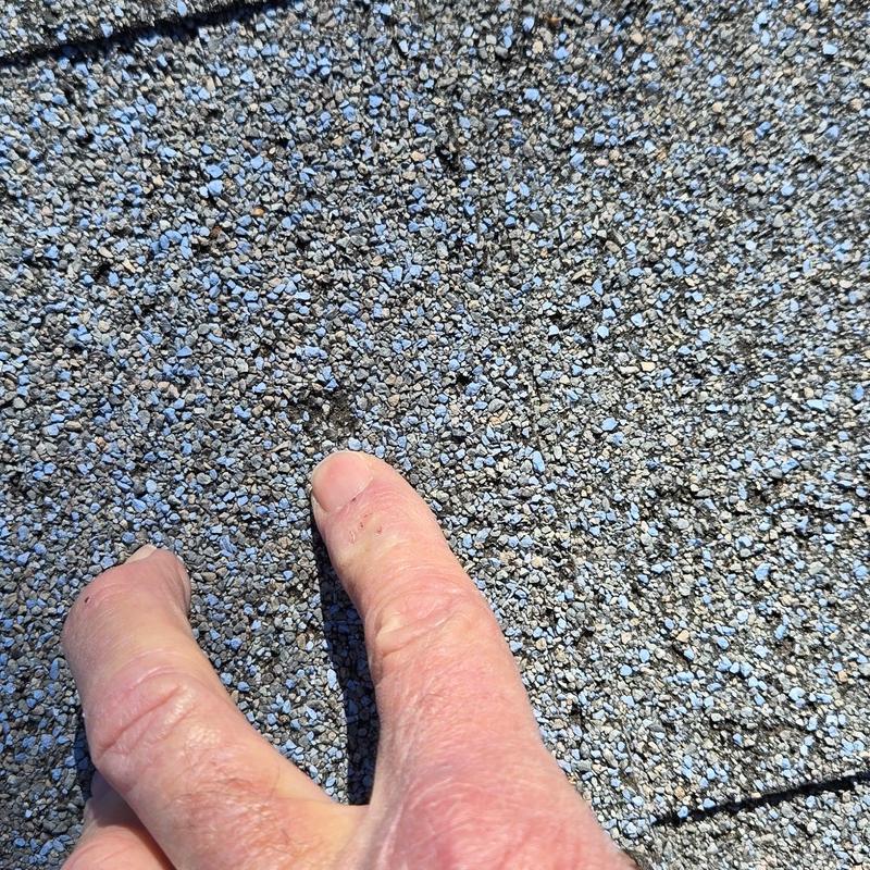 Roof shingles with hail damage close-up and hand point