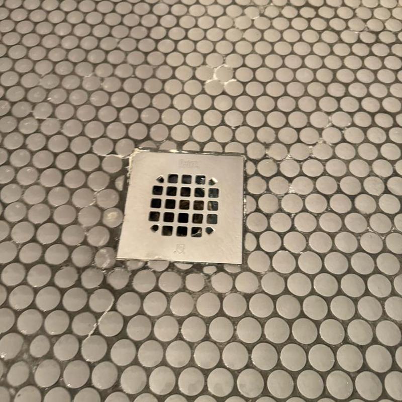 Shower drain with square metal grate in tiled floor Shower drain with square metal grate in tiled floor