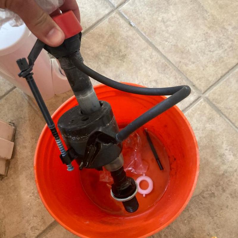 Toilet fill valve held above orange bucket on tile floor