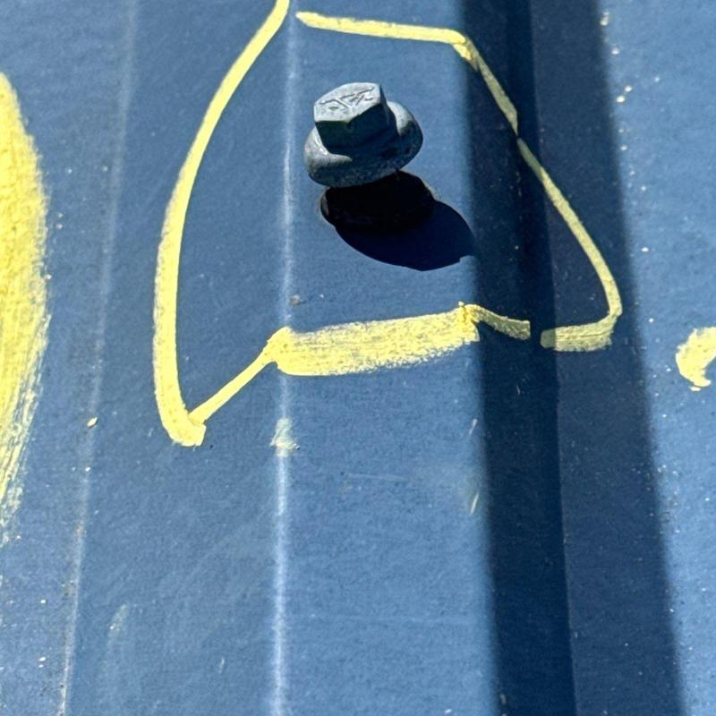 Metal roof screw with hail damage and yellow marking