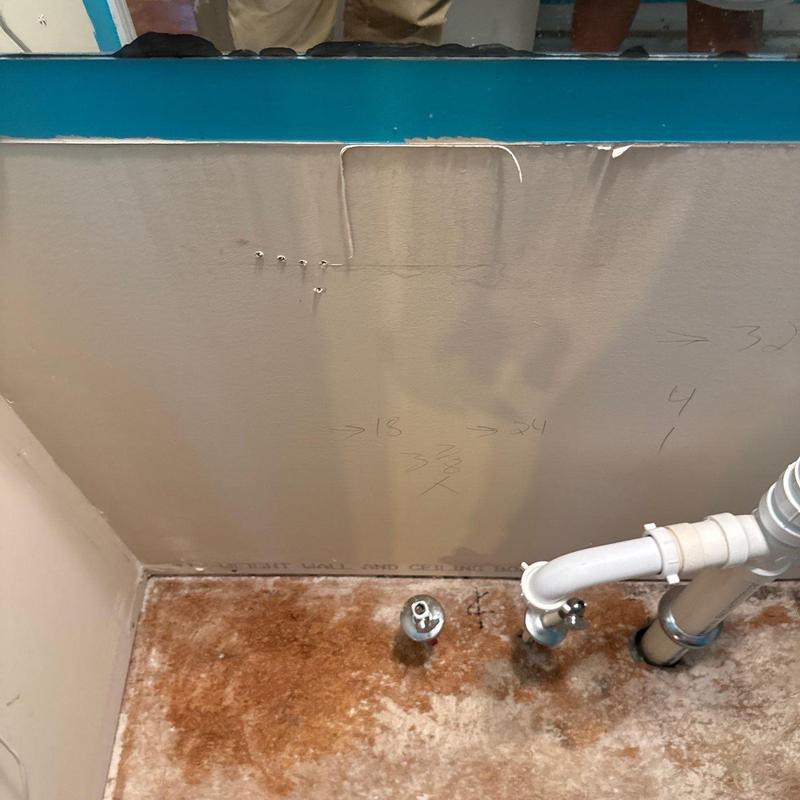 Bathroom sink plumbing with wall damage and mold stains