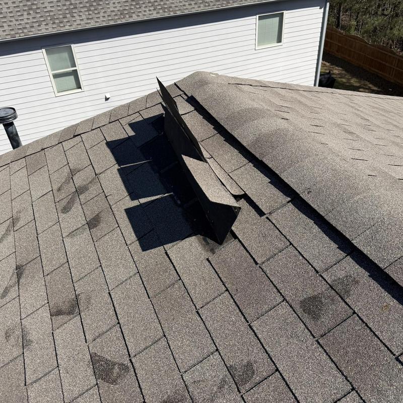 Damaged roof shingles with lifted ridge vent section