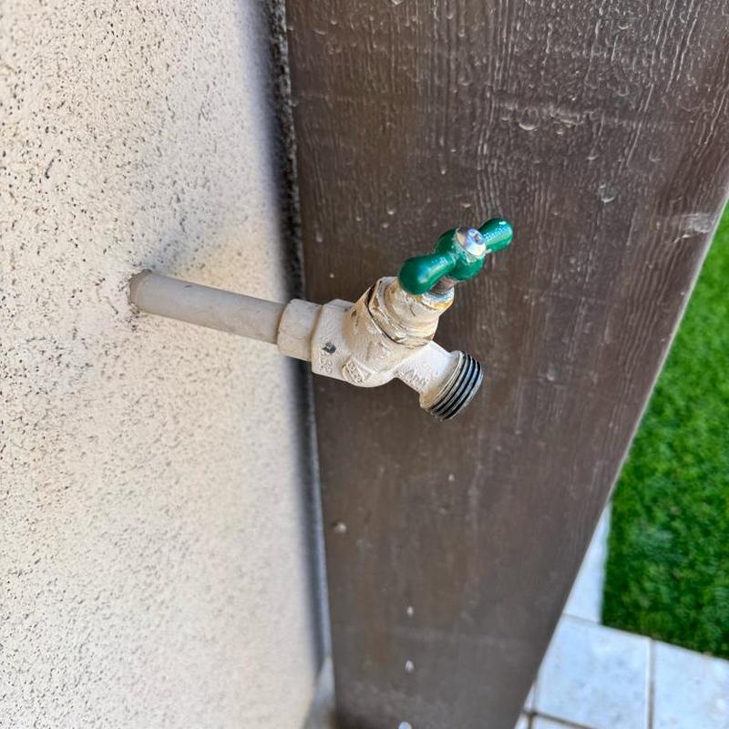Hose bib with green handle on exterior wall