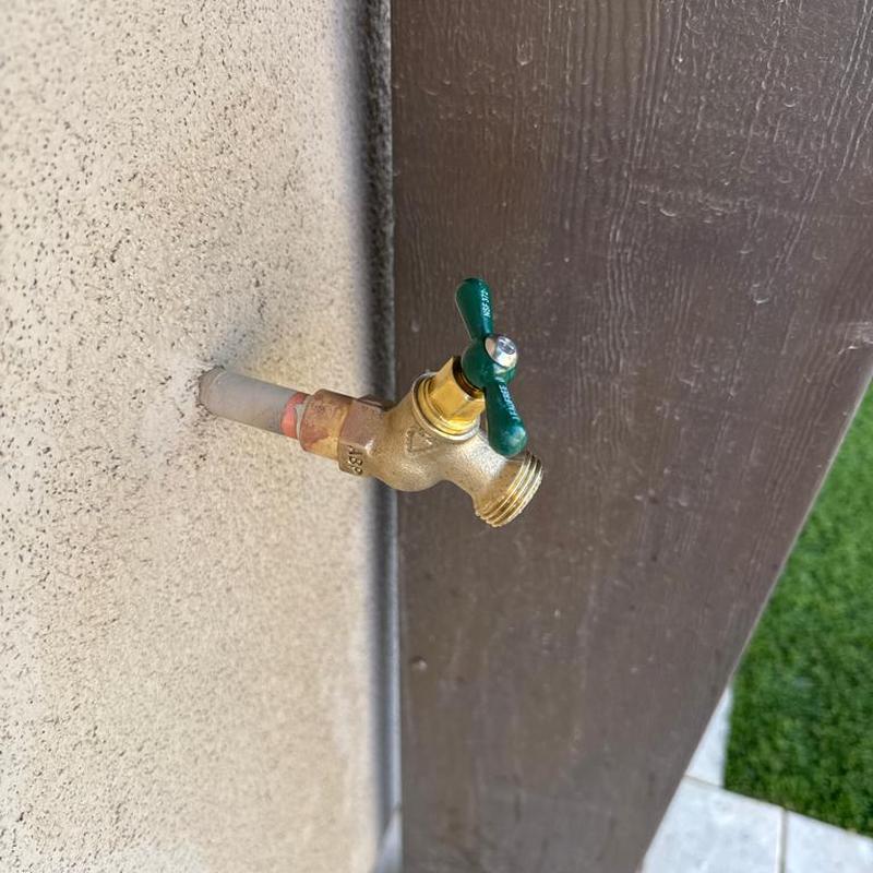 Outdoor hose bib with green handle on stucco wall