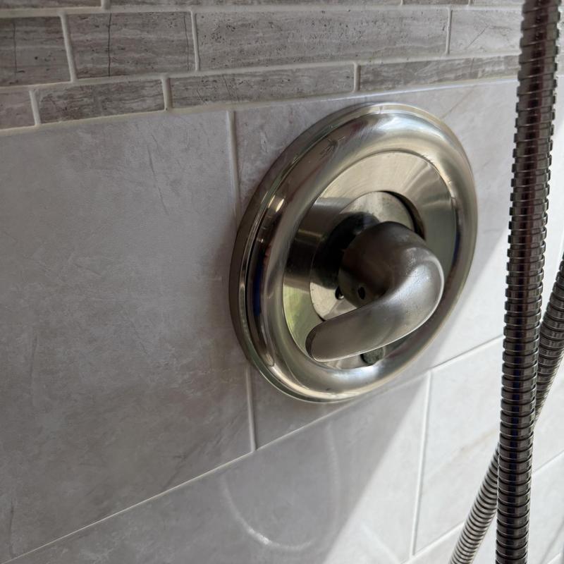 Delta shower valve handle on tiled wall with hose