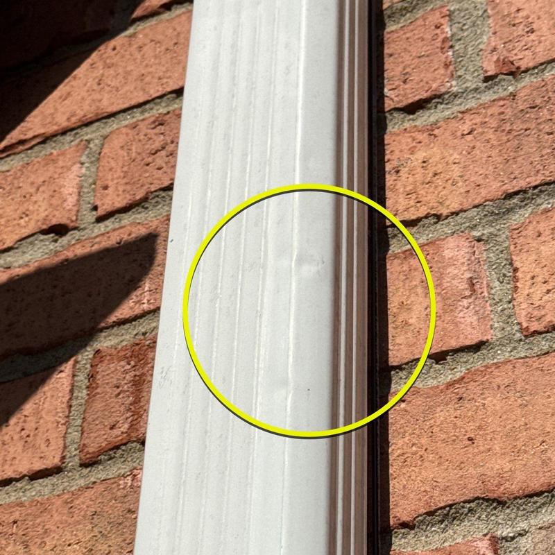 Downspout dent on white gutter system against brick wall