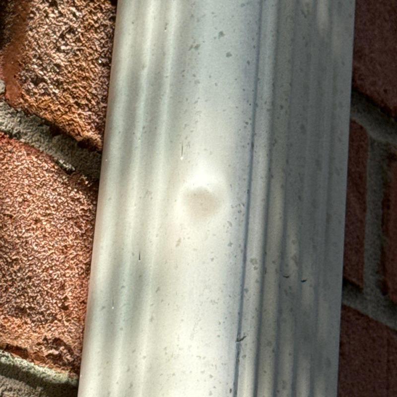Metal gutter dent from hail damage on brick wall