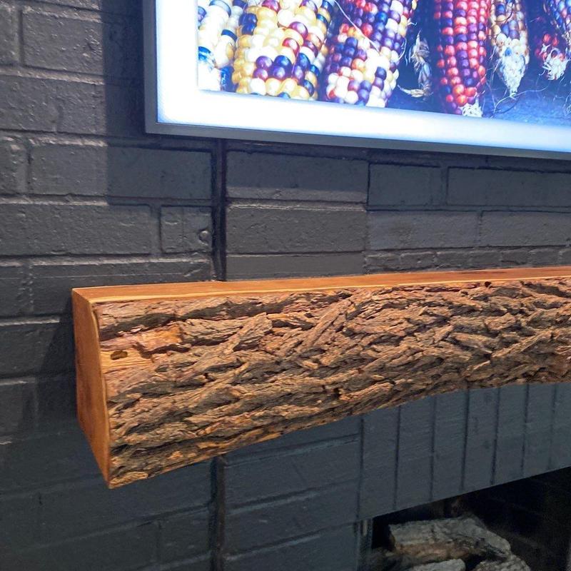 Rustic wooden fireplace mantel on black brick wall