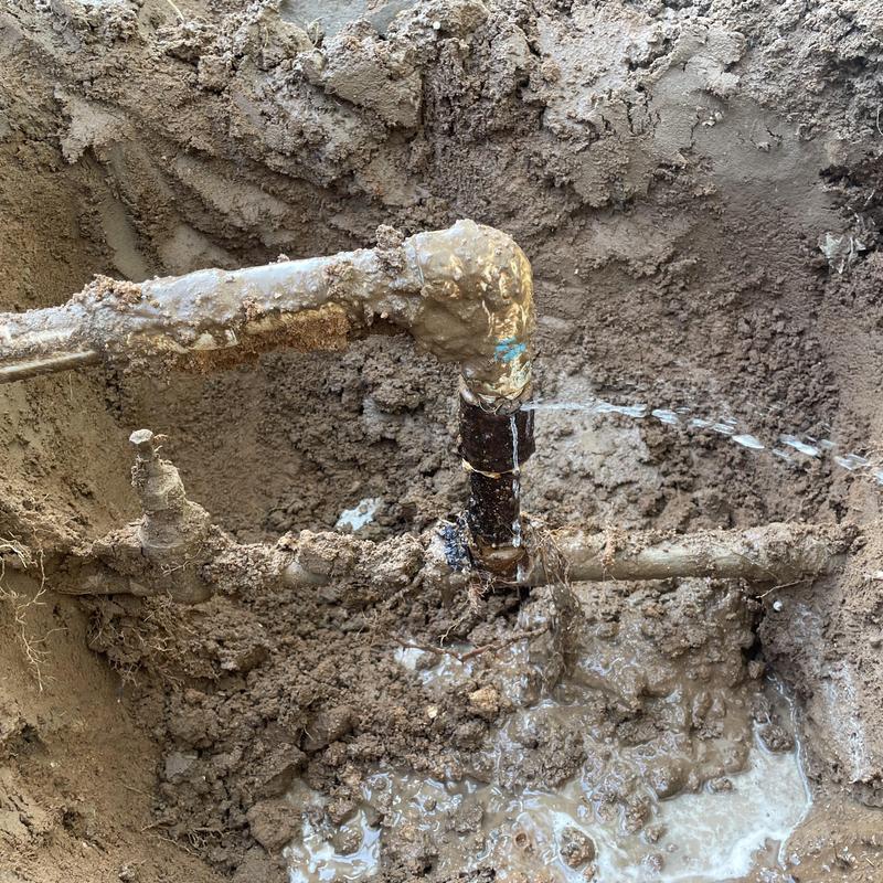 Galvanized pipe water leak spraying in muddy soil excavation