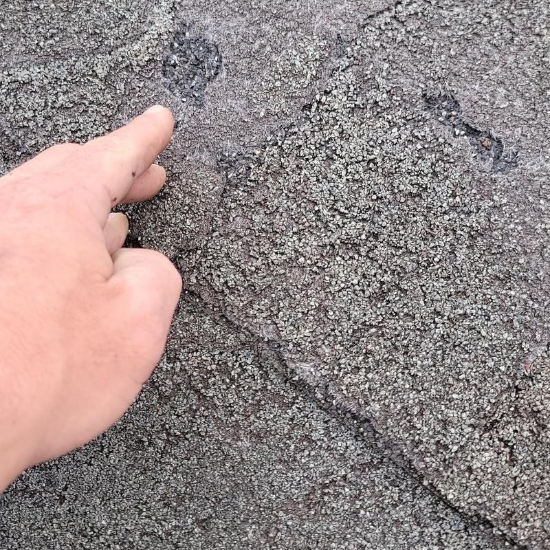 Roof shingles hail damage close-up with hand pointing