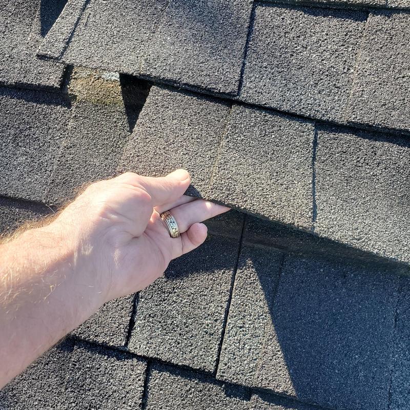Asphalt roof shingles lifted by hand showing damage