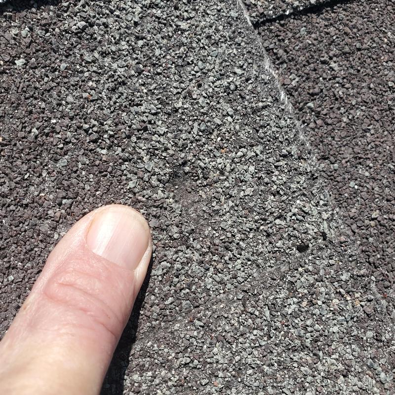 Asphalt shingle close-up showing hail damage with finger for scale