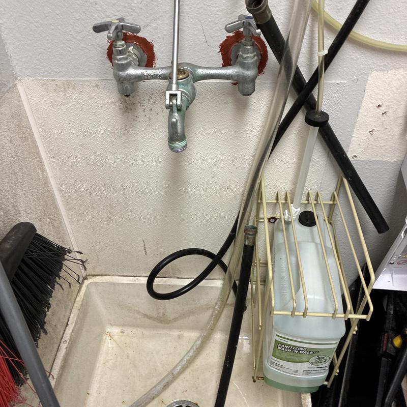 Commercial mop sink faucet with hoses and cleaning supplies