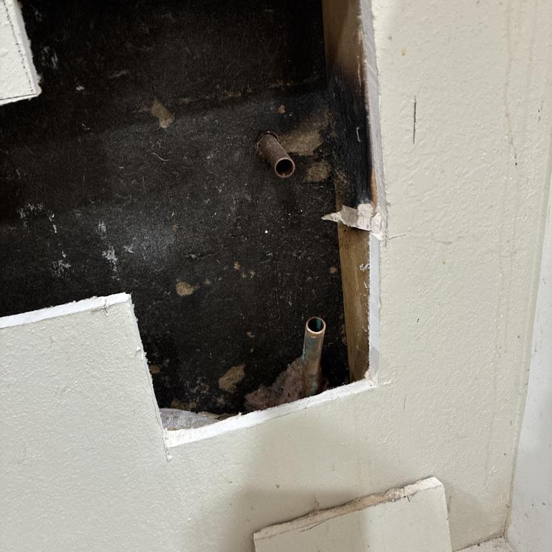 Copper plumbing pipes behind kitchen wall panel