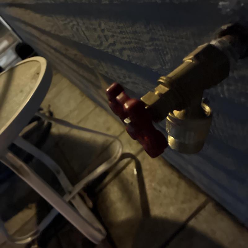 Hose bib valve with red handle on exterior wall