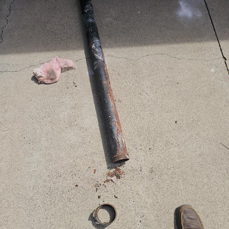 Cast iron drain pipe with rust and cracks on concrete