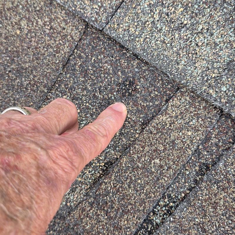 Roof shingles with hail damage spot marked by finger