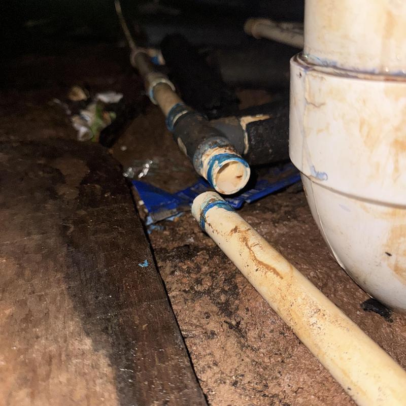 PVC pipe fitting under home with leak repair prep