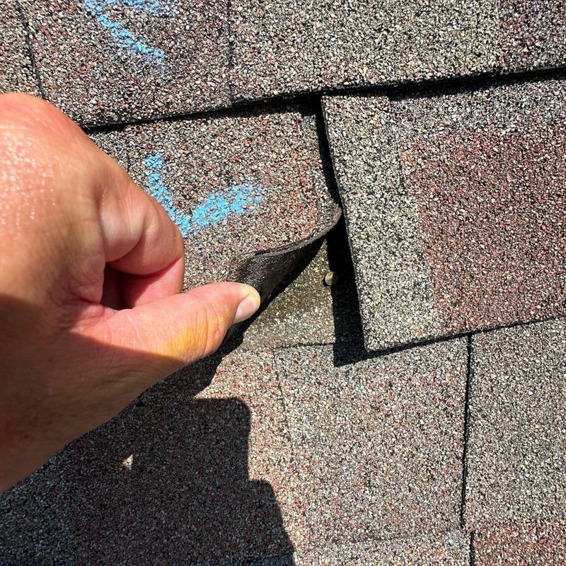 Asphalt roof shingles lifted to inspect hail damage