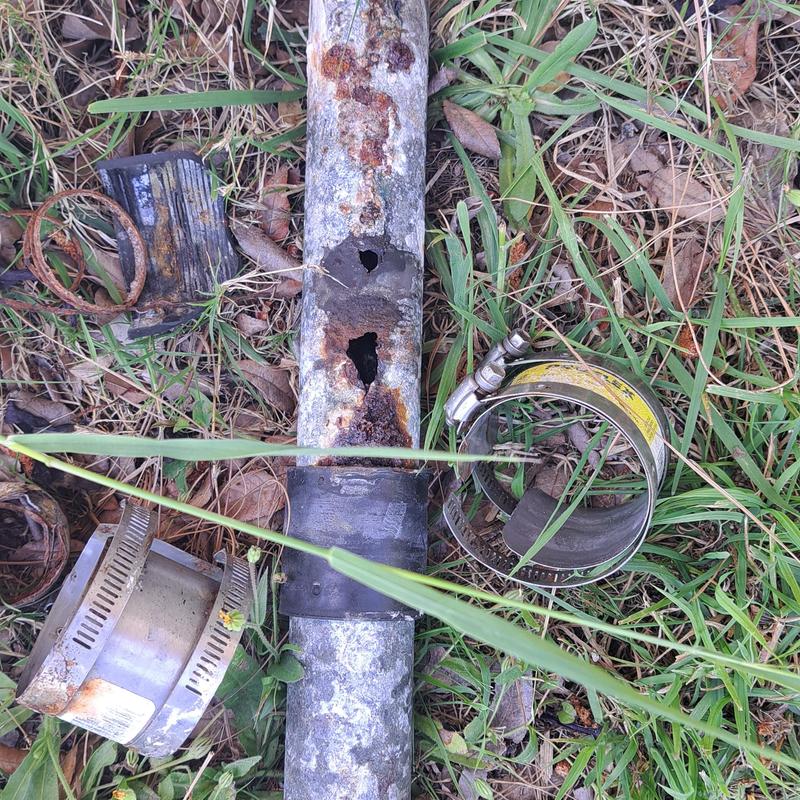 Rusty corroded metal pipe with holes in grass