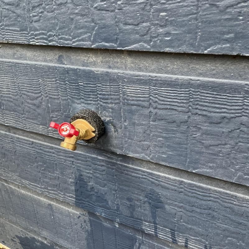 Brass outdoor water spigot with red handle on siding
