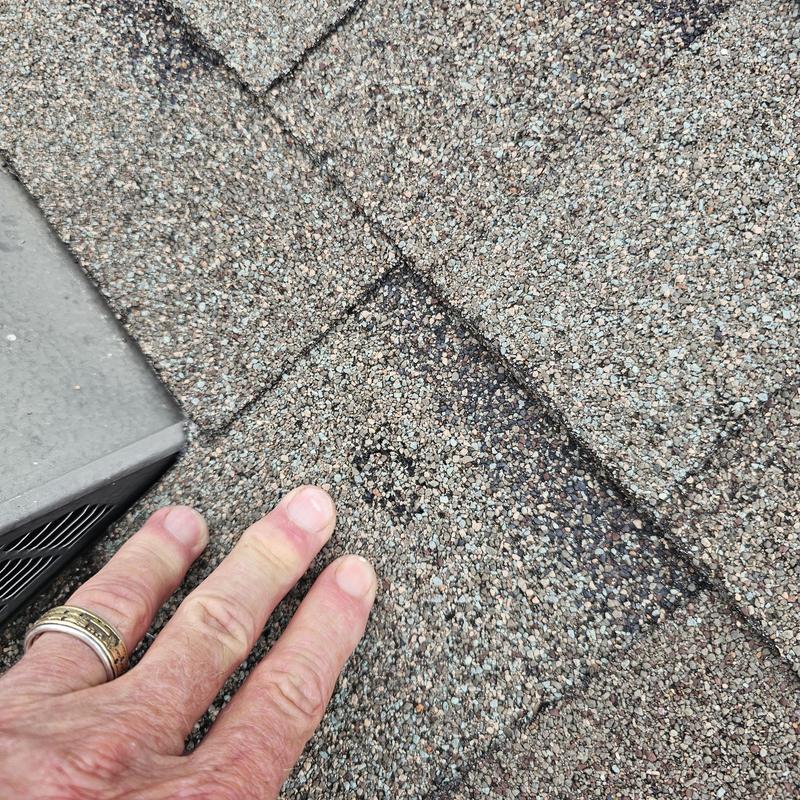 Asphalt roof shingles with visible hail damage near AC unit
