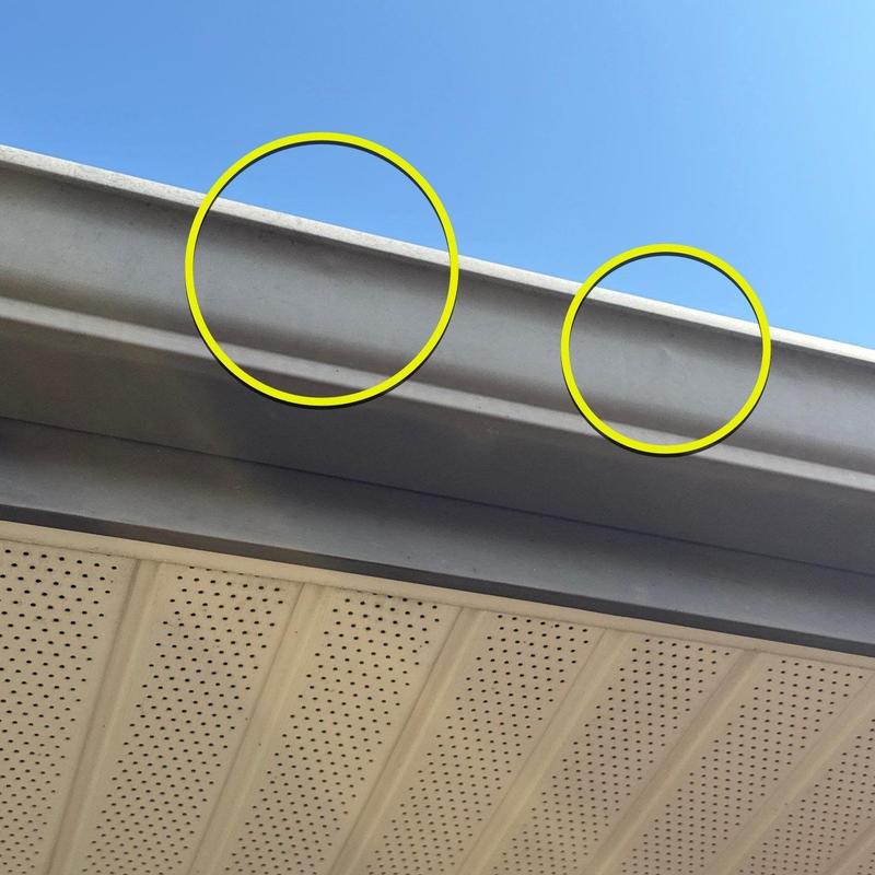 Metal gutter with hail damage dents under blue sky