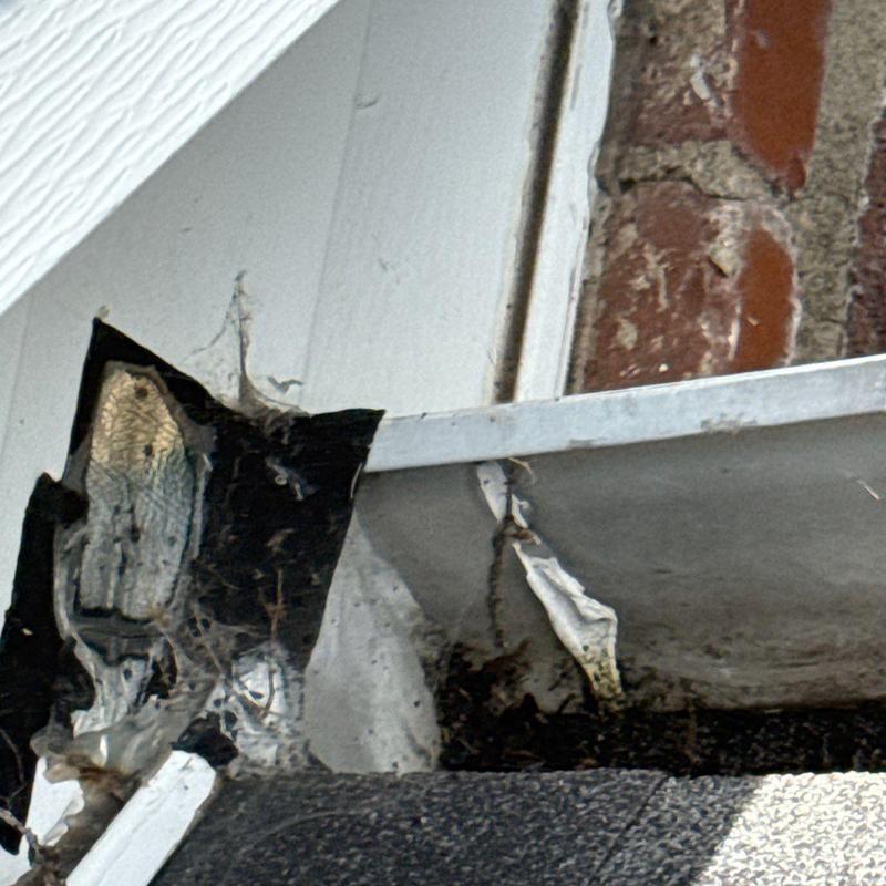 Roof flashing with torn and damaged sealant near brick wall