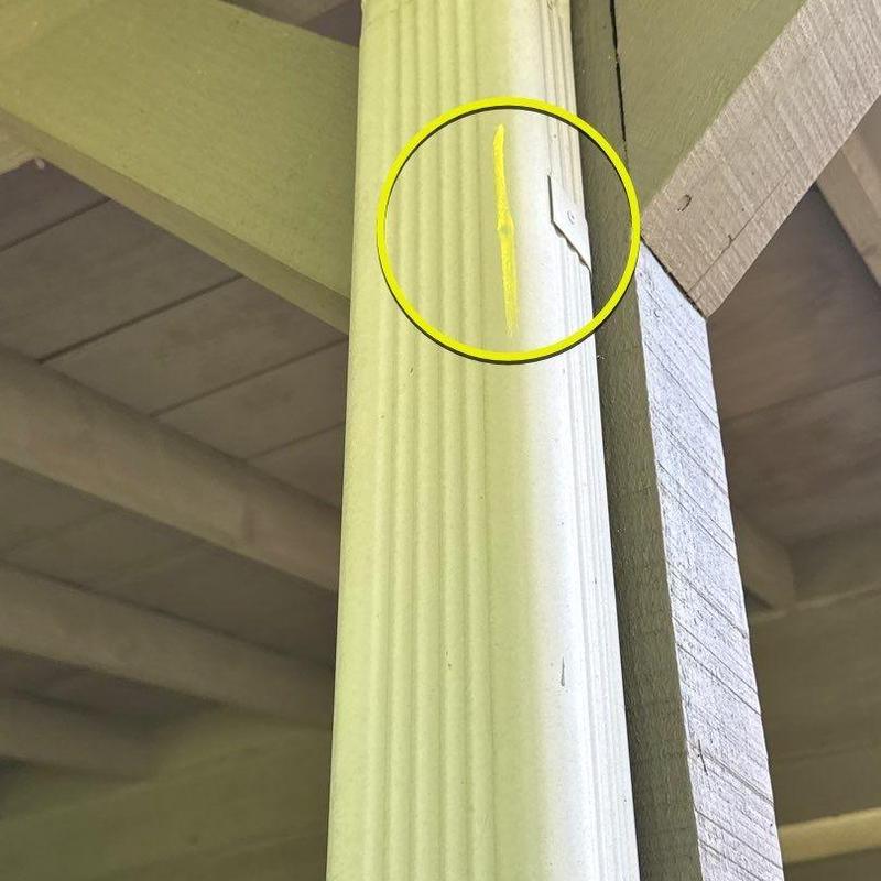 Vinyl downspout with dent damage circled in yellow