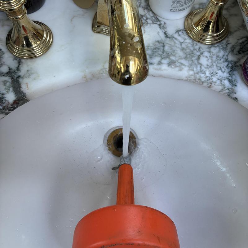 Sink drain clearing with plumbing auger in bathroom sink
