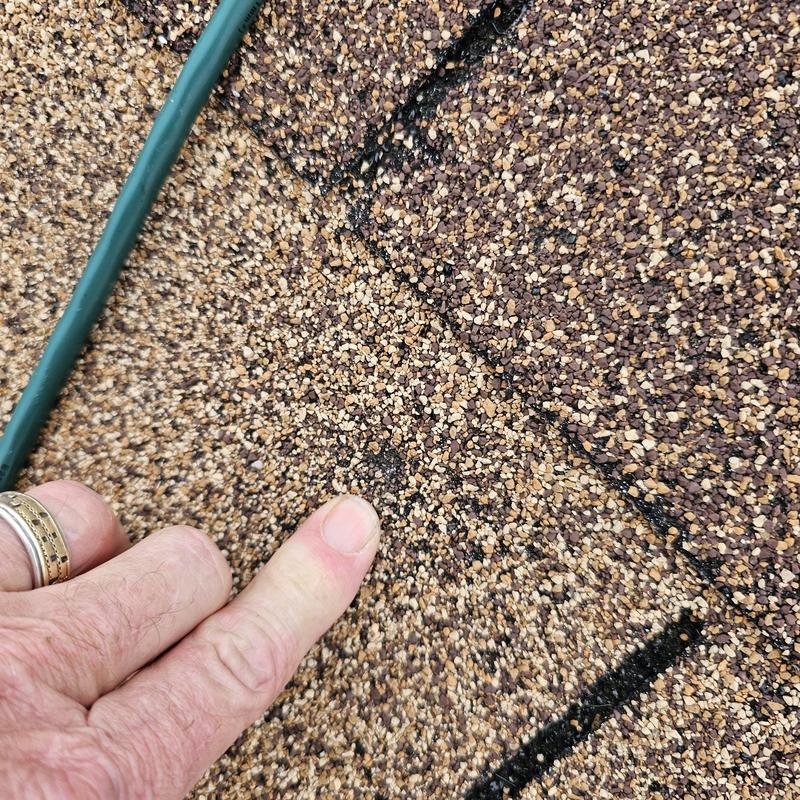 Asphalt shingle roof hail damage close-up with finger pointing