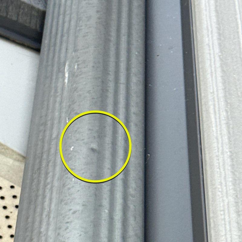 Metal downspout dent with circled hail damage close-up