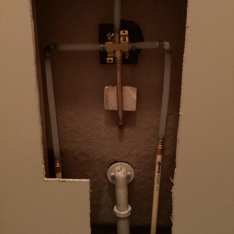 Shower valve plumbing exposed behind drywall cutout