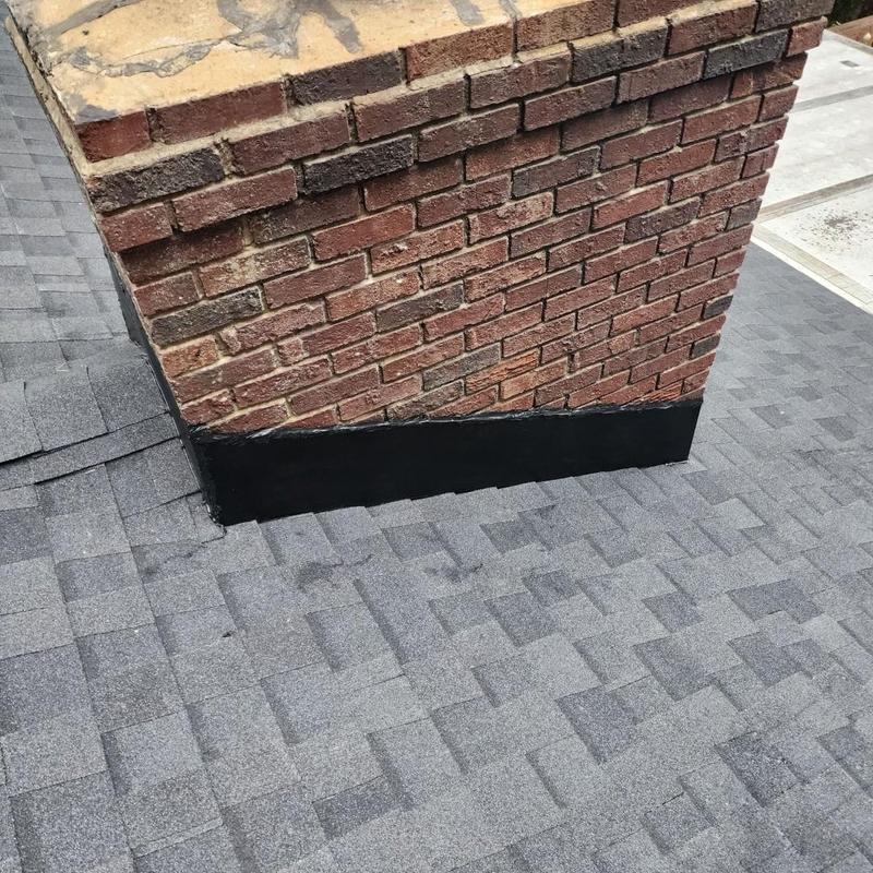 Roof chimney flashing with black sealant on gray shingles