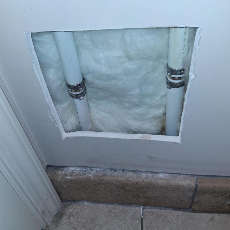 PVC water pipes with repair clamps behind drywall panel