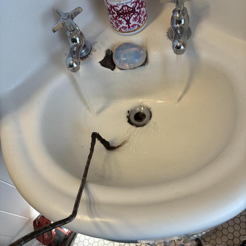 Bathroom sink drain clearing with plumbing auger in use