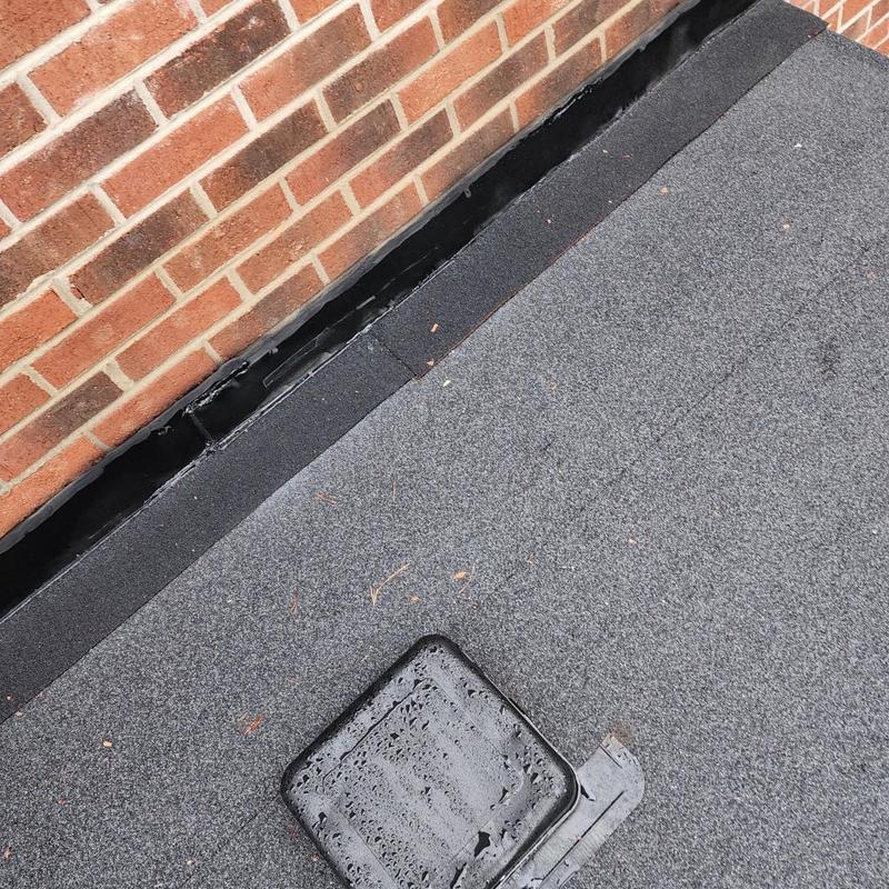 Modified bitumen flat roof with drain near brick wall