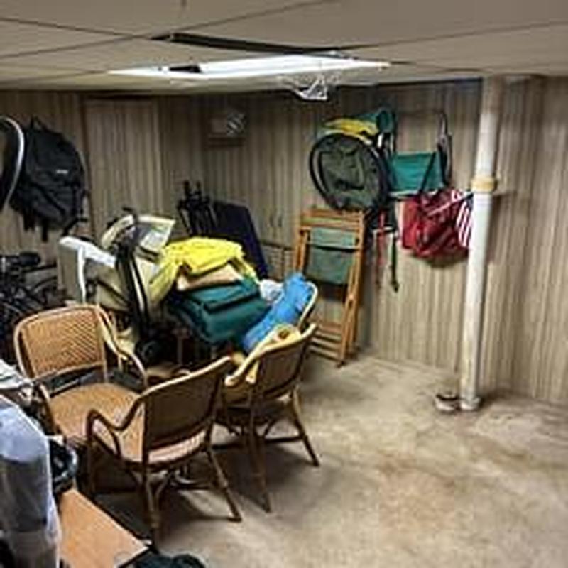 Basement main line pipe near cluttered chairs and stored items